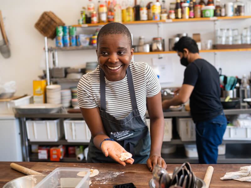 Woman in industrial kitchen holding a dumpling in one hand